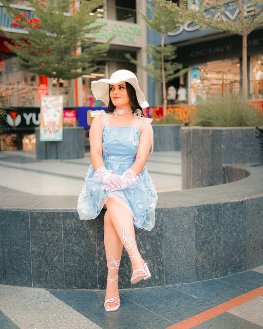 Woman in blue dress and white hat seated in a city setting